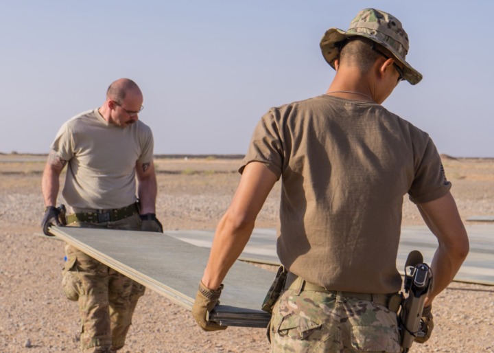 Tech. Sgt. Dan Zimmerman (back) and Senior Airman Thet Tun (front) carry a piece of AM2 matting material, Camp Dwyer, Afghanistan, July, 12, 2016. Zimmerman and Tun constructed a 100’ x 100’ helicopter landing zone out of AM2 matting to support the medical facility at Camp Dwyer. (Courtesy photo by 451 Air Expeditionary Support Squadron)