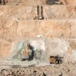 Open-pit mine with terraced benches and heavy equipment including excavators and dump trucks.
