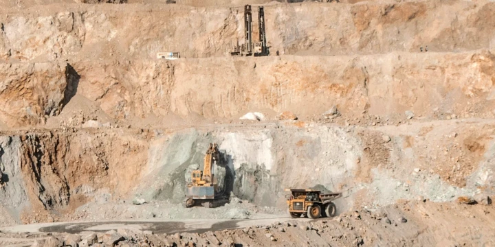 Open-pit mine with terraced benches and heavy equipment including excavators and dump trucks.