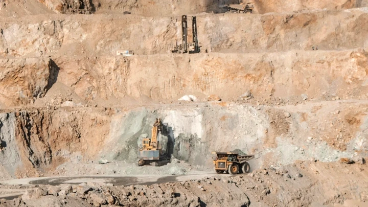 Open-pit mine with terraced benches and heavy equipment including excavators and dump trucks.