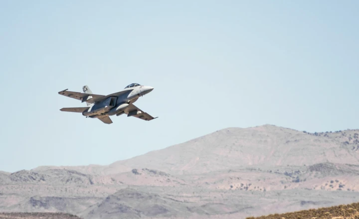 F-15 Eagle fighter jet in flight over a desert landscape with mountains in the distance.
